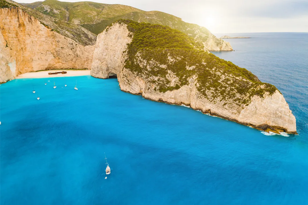 Navagio Beach in Zakynthos with turquoise water and boats anchored near the rocky shore.