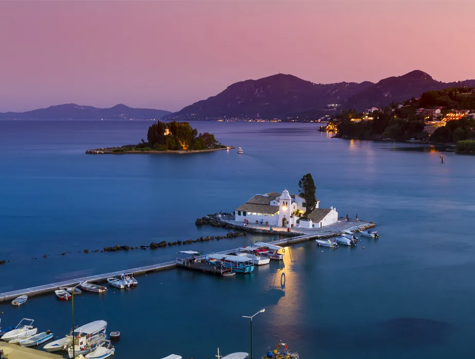 Corfu harbor at dusk with small boats and the Vlacherna Monastery on a tiny island.