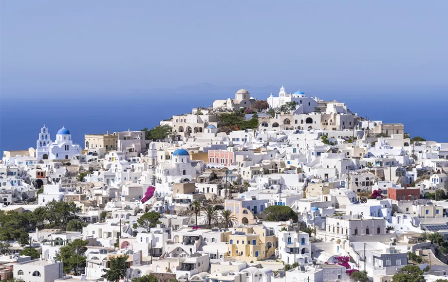 Ville de Santorin avec des bâtiments blancs et des dômes bleus surplombant la mer Égée par temps clair.
