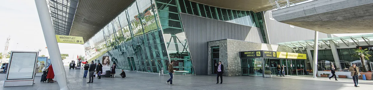Tirana International Airport arrivals area with travelers and modern glass architecture for car rental.