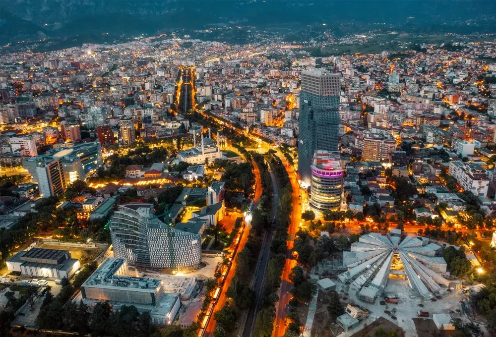 Tirana cityscape at dusk with illuminated streets and modern buildings for car rental services.