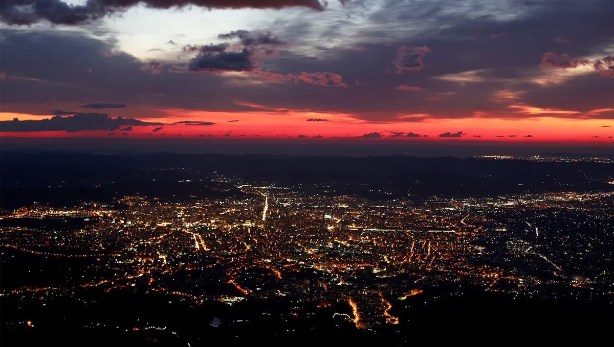 Cityscape at sunset with glowing streetlights and a vibrant red and purple sky above the urban area.