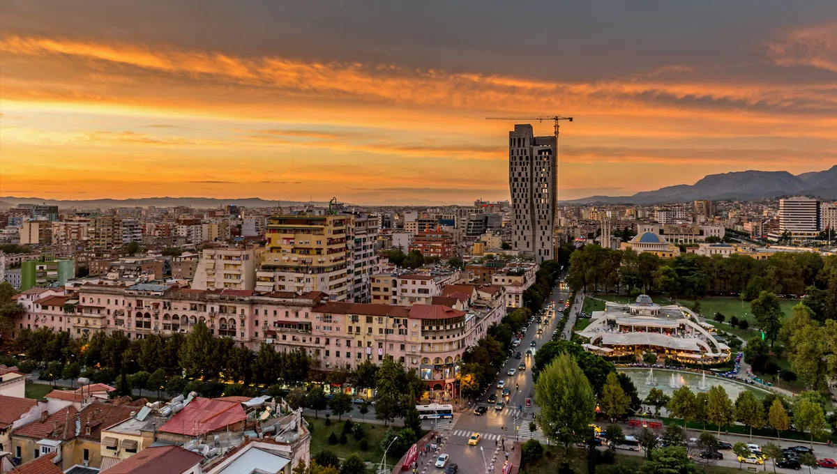 Tirana cityscape at sunset with busy streets and tall buildings in Albania car rental area.