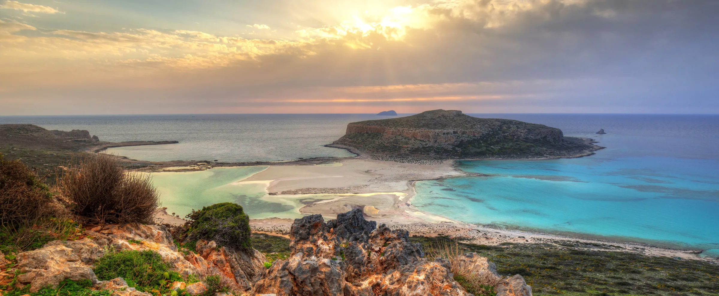 Balos Lagoon in Crete with turquoise waters and rocky coastline under cloudy sky at sunset.