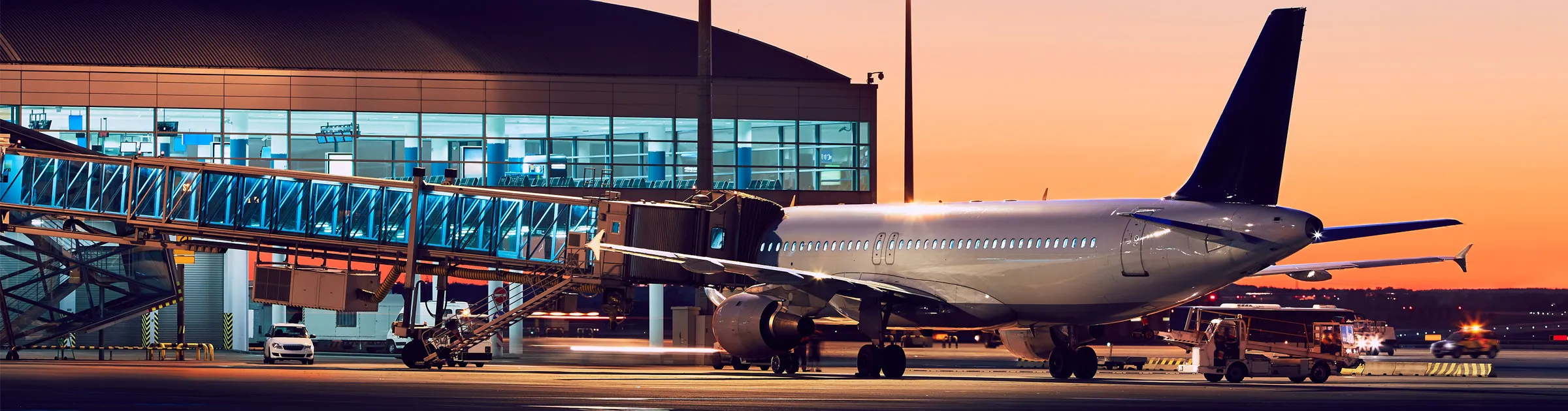Aereo commerciale ancorato al gate dell'aeroporto con passerella d'imbarco al tramonto.