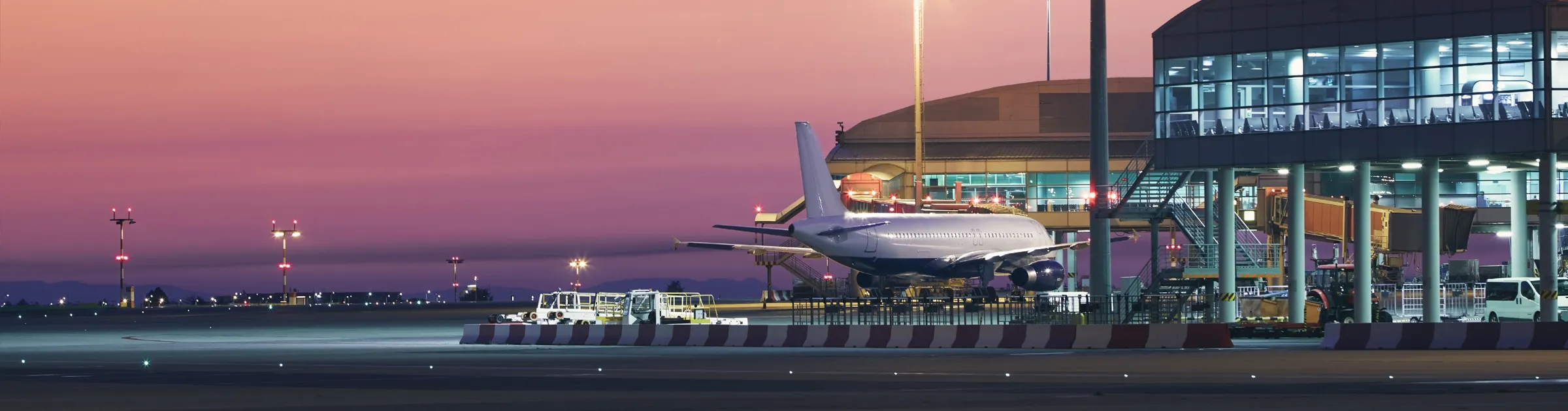 Airport runway with a parked airplane and terminal building during sunset.
