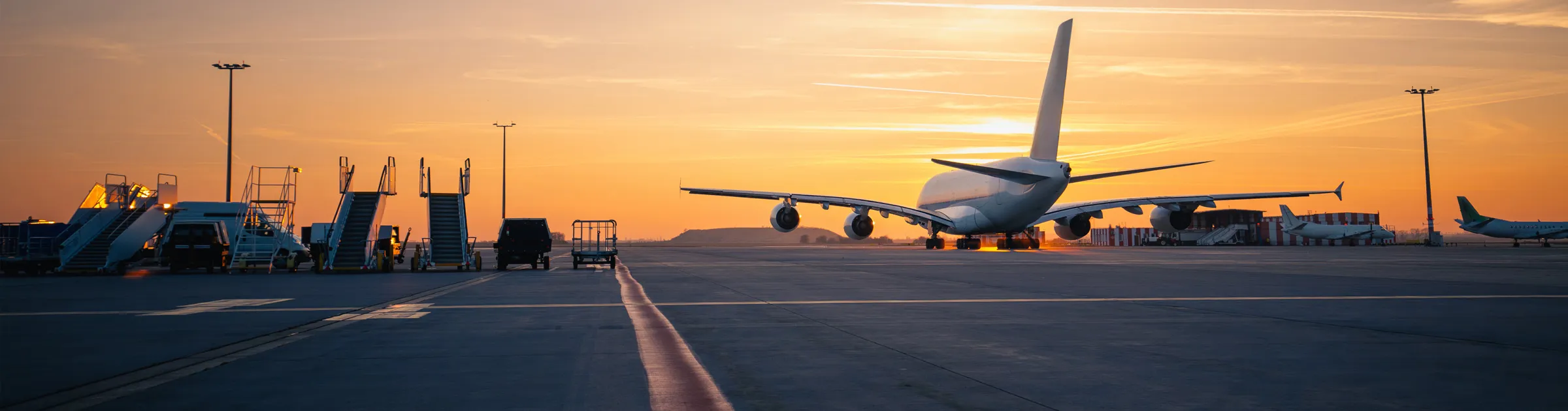 Airplane parked on the runway at sunset with boarding stairs and service vehicles nearby at the airport.