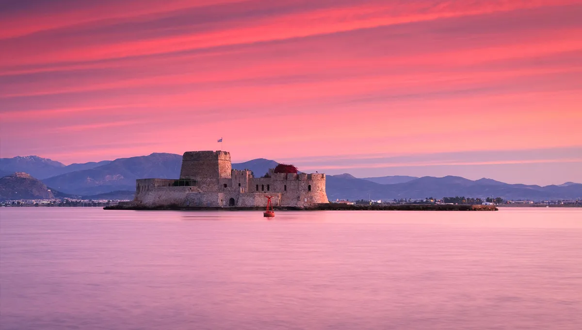 Bourtzi Castle in Nafplio with a pink sunset sky and calm water around the small fortress island.