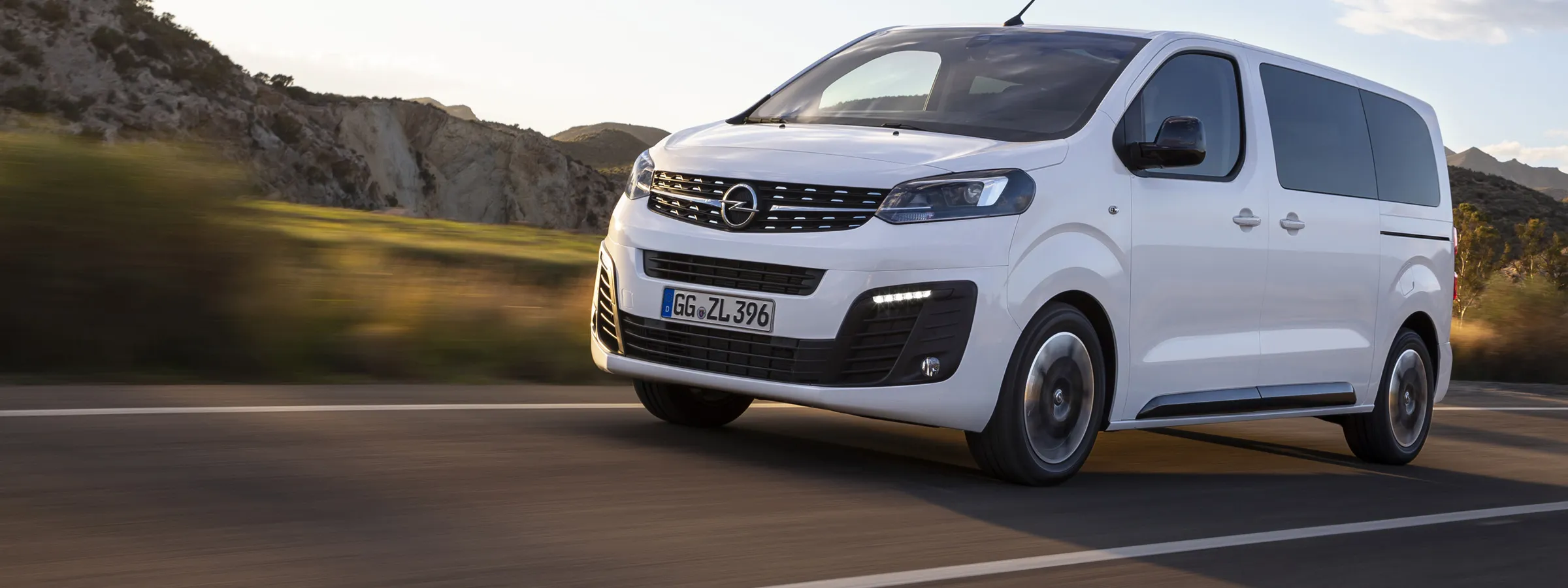 Opel van rental driving on open road with hills in the background, ideal for group travel or cargo.