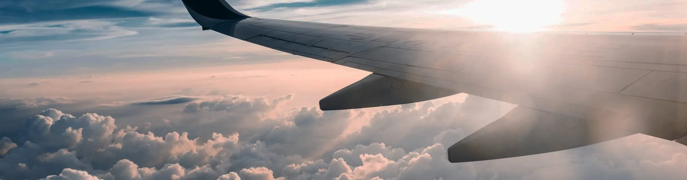 Vleugel van vliegtuig boven de wolken tijdens zonsondergang, ideaal voor autoverhuur op luchthavens.