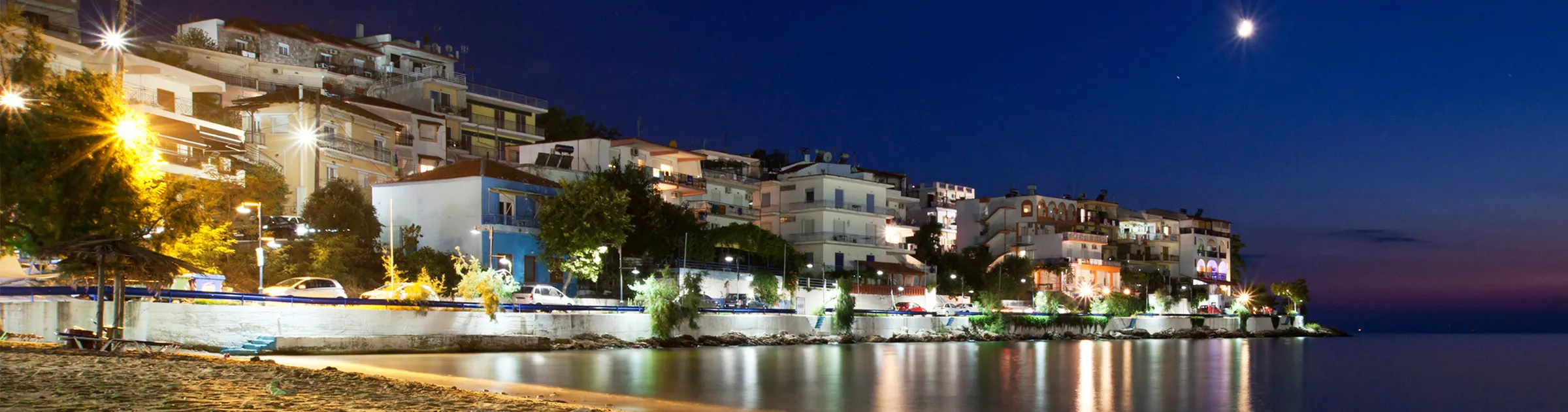 Seaside town illuminated at night with calm waters and beach by the shore.