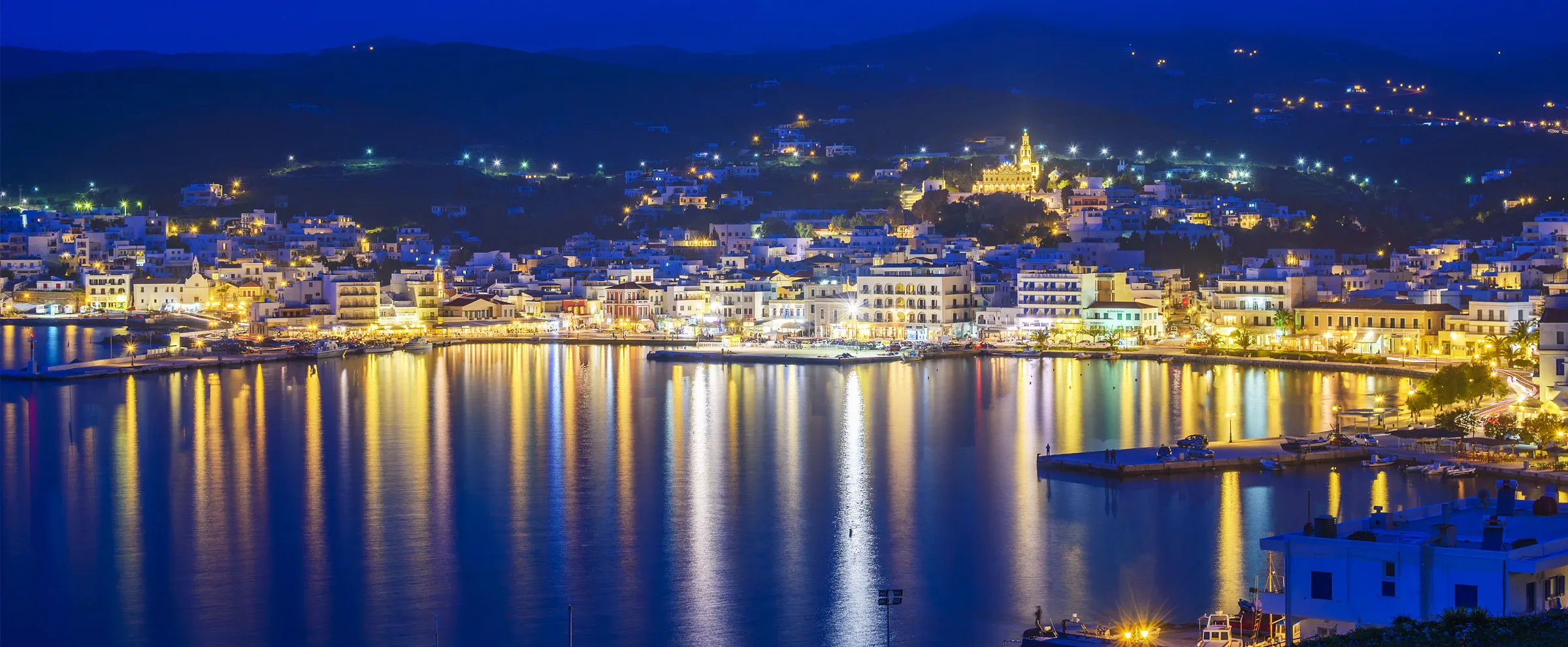 Vista notturna dell'isola di Poros con edifici illuminati riflessi sull'acqua calma.