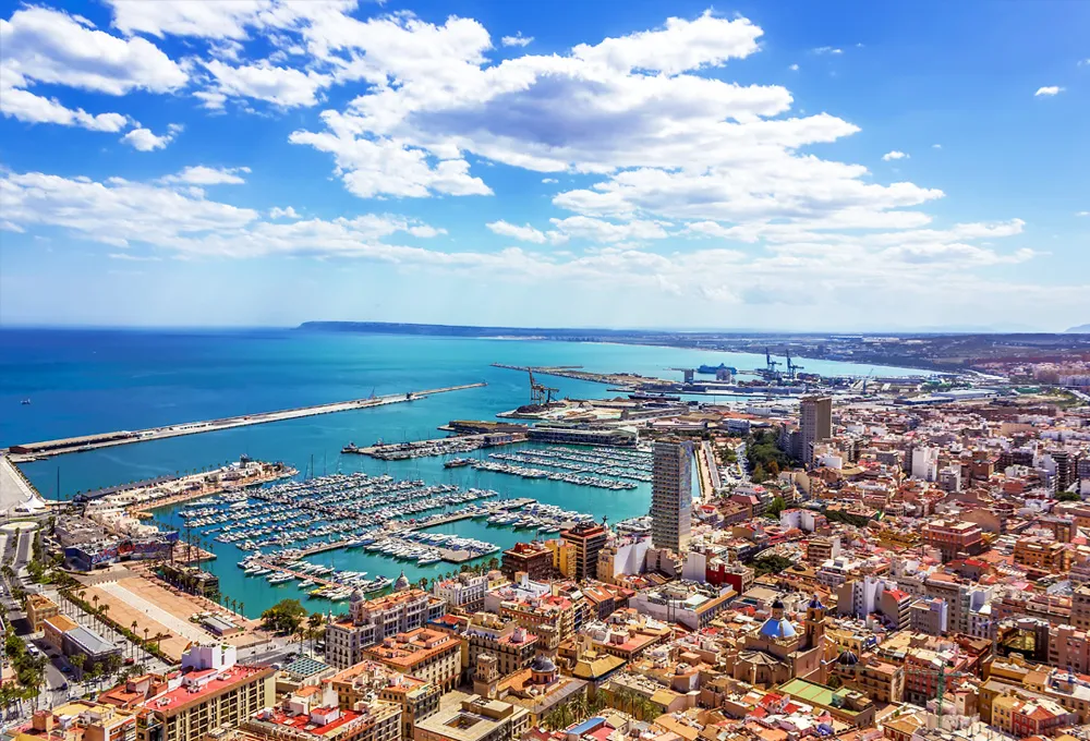 Orașul de coastă Alicante cu port de agrement și bărci ancorate sub un cer parțial înnorat pentru închiriere auto.