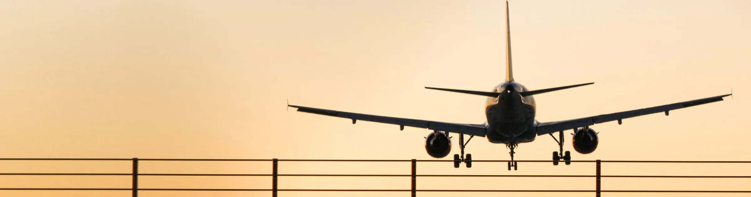 Passenger plane landing at sunset with runway fence in view for airport car rental services.
