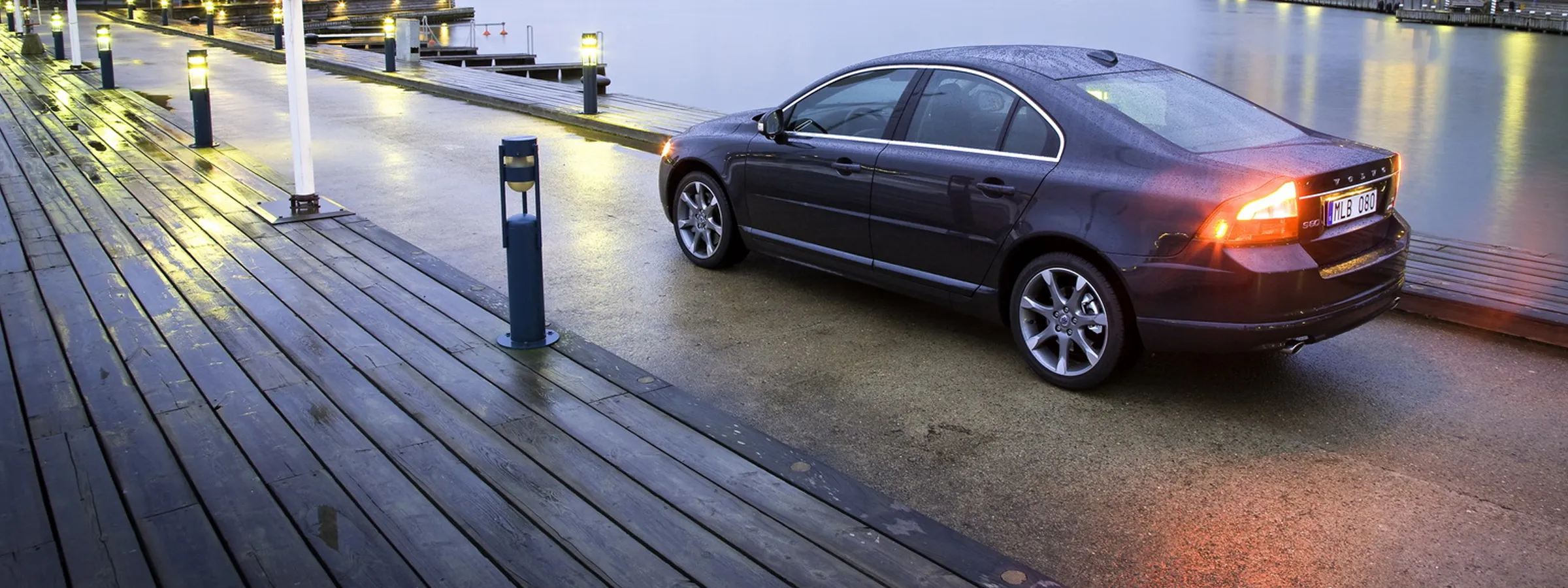 Volvo S80 sedan de lux parcat pe un dig umed în amurg pentru închiriere auto.