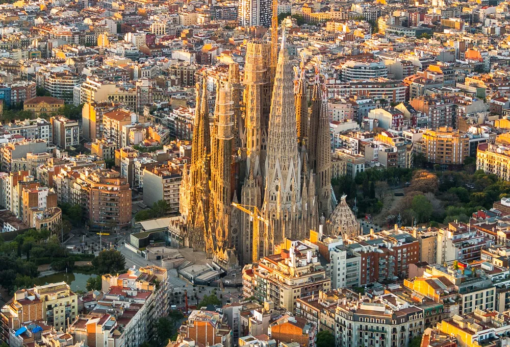 Vedere aeriană a Barcelonei cu bazilica Sagrada Familia și clădiri înconjurătoare la apus.