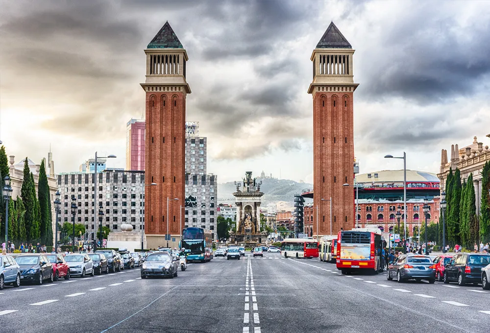 Aleea largă cu trafic și două turnuri venețiene în Piața Spaniei din Barcelona, Spania.