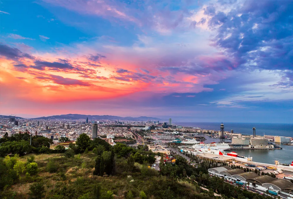 Peisaj urban din Barcelona și port la apus cu cer colorat și clădiri de-a lungul coastei.