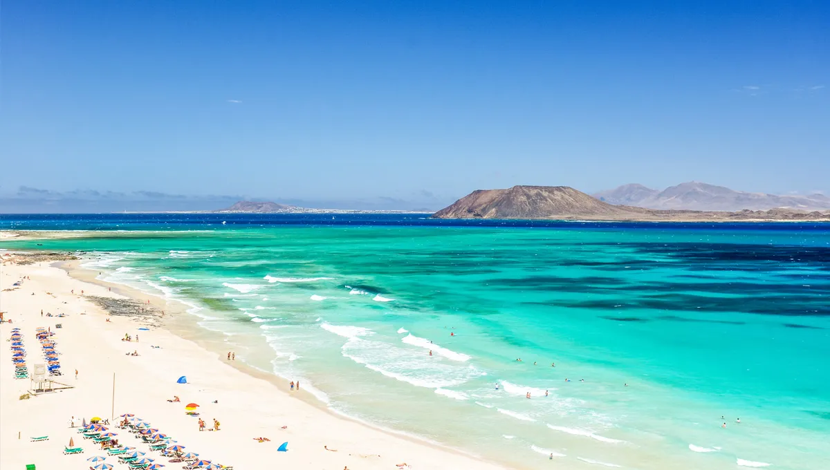 Plaja Lanzarote cu ape turcoaz și oameni care se bucură de soare și valuri pe coastă.