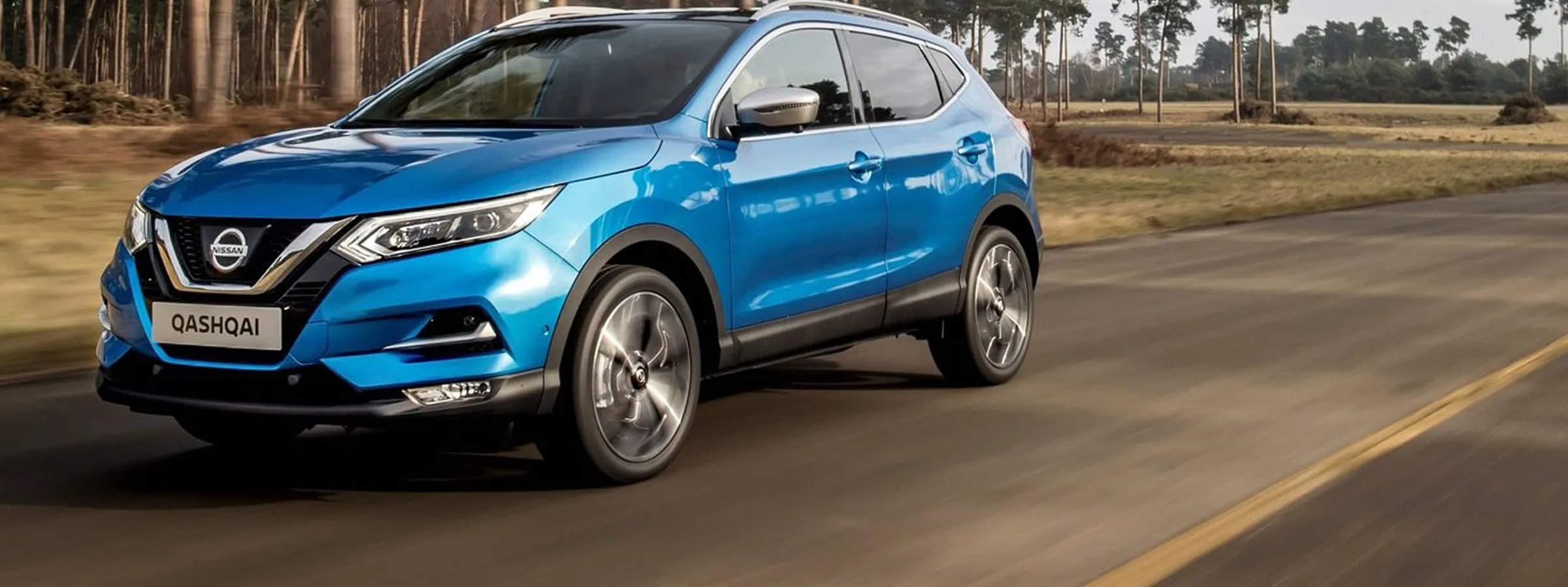 Nissan Qashqai SUV compact albastru în mișcare pe drum rural pentru închiriere auto.