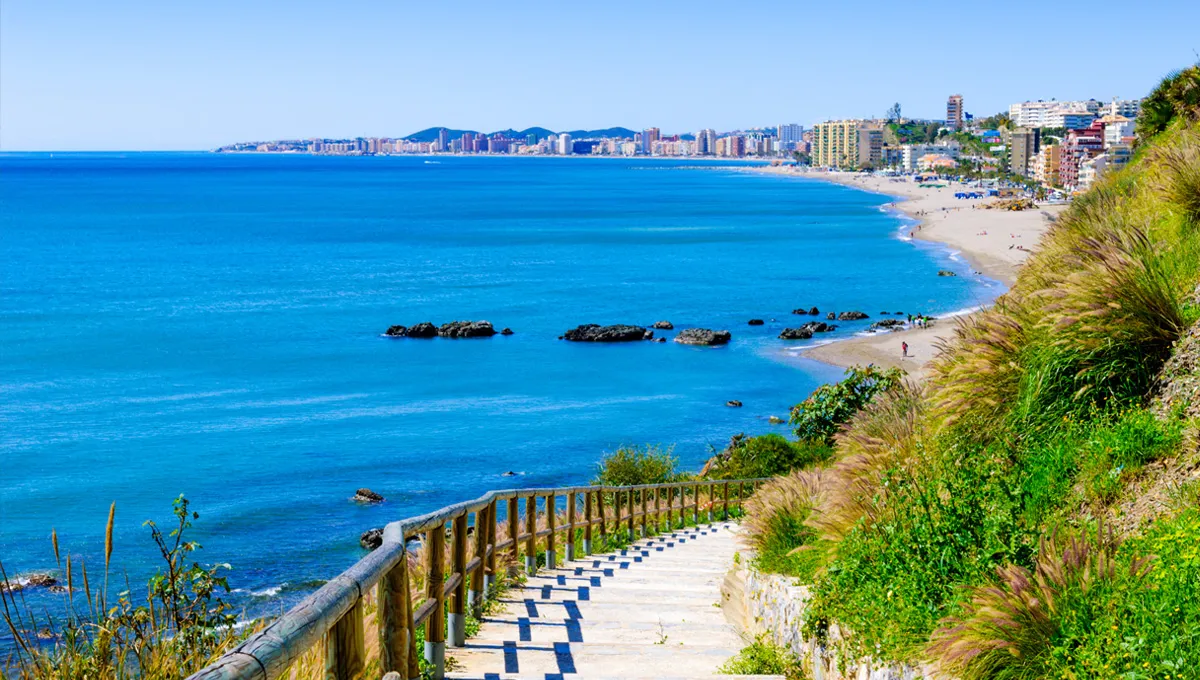 Coasta Benidorm cu scări spre plajă, mare albastră și oraș pentru închiriere auto.