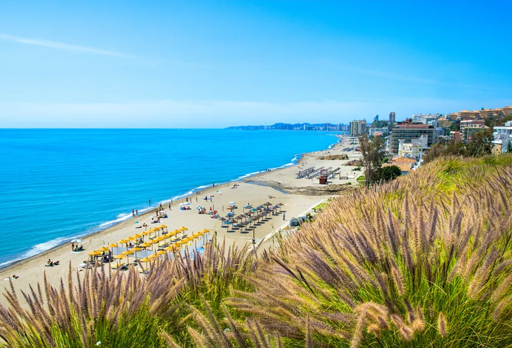 Coasta din Benalmádena cu plajă însorită, umbrele și clădiri de-a lungul țărmului în Spania.