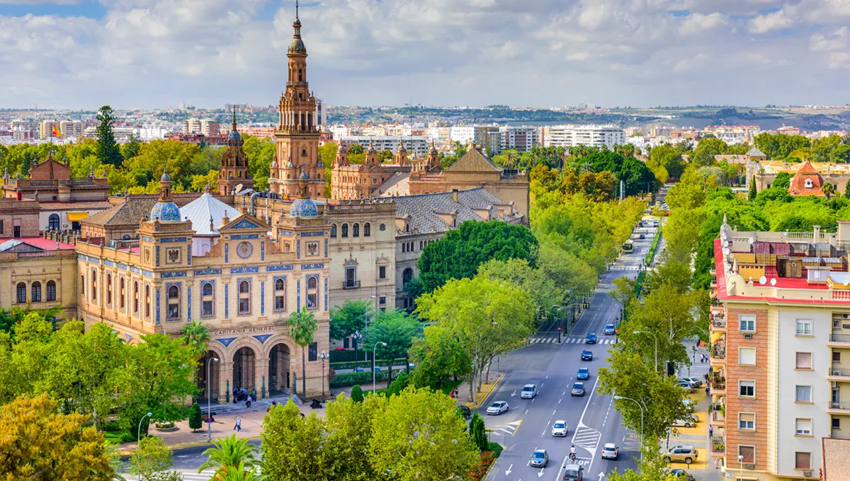 Seville cityscape with historic buildings and a busy road lined with trees for car rental access.