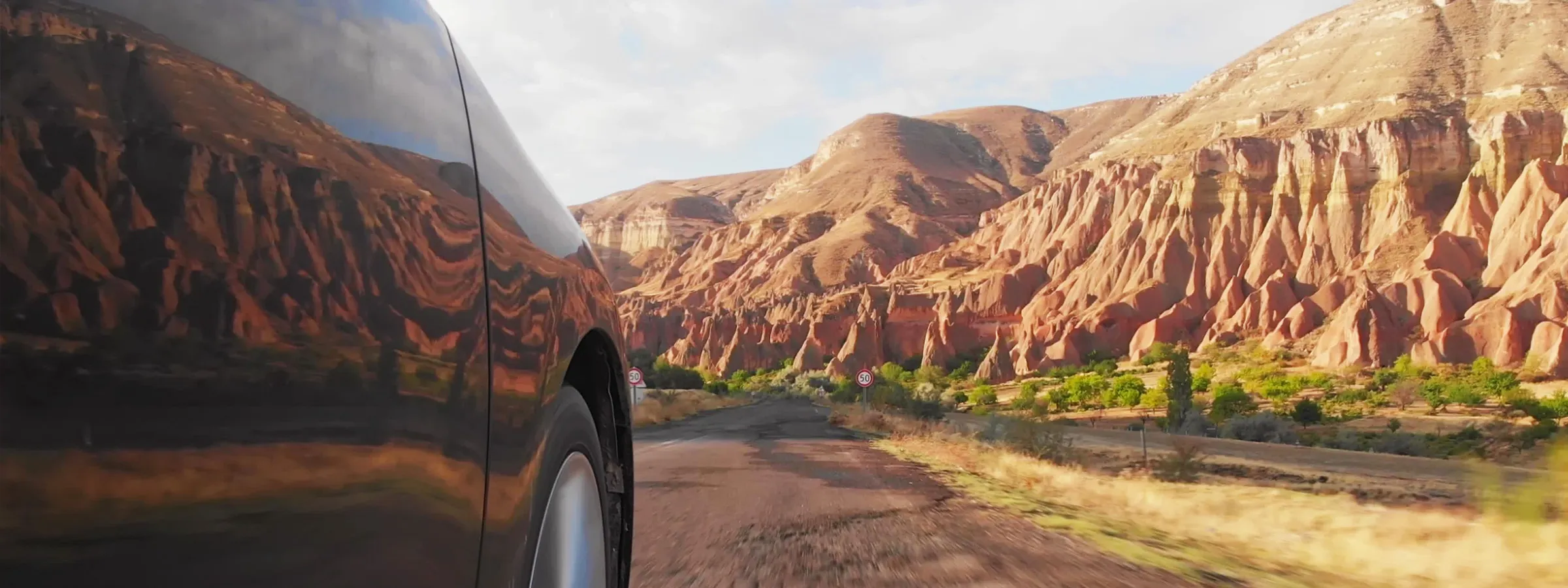 Black rental car driving on a scenic road with unique rock formations and hills in the background.