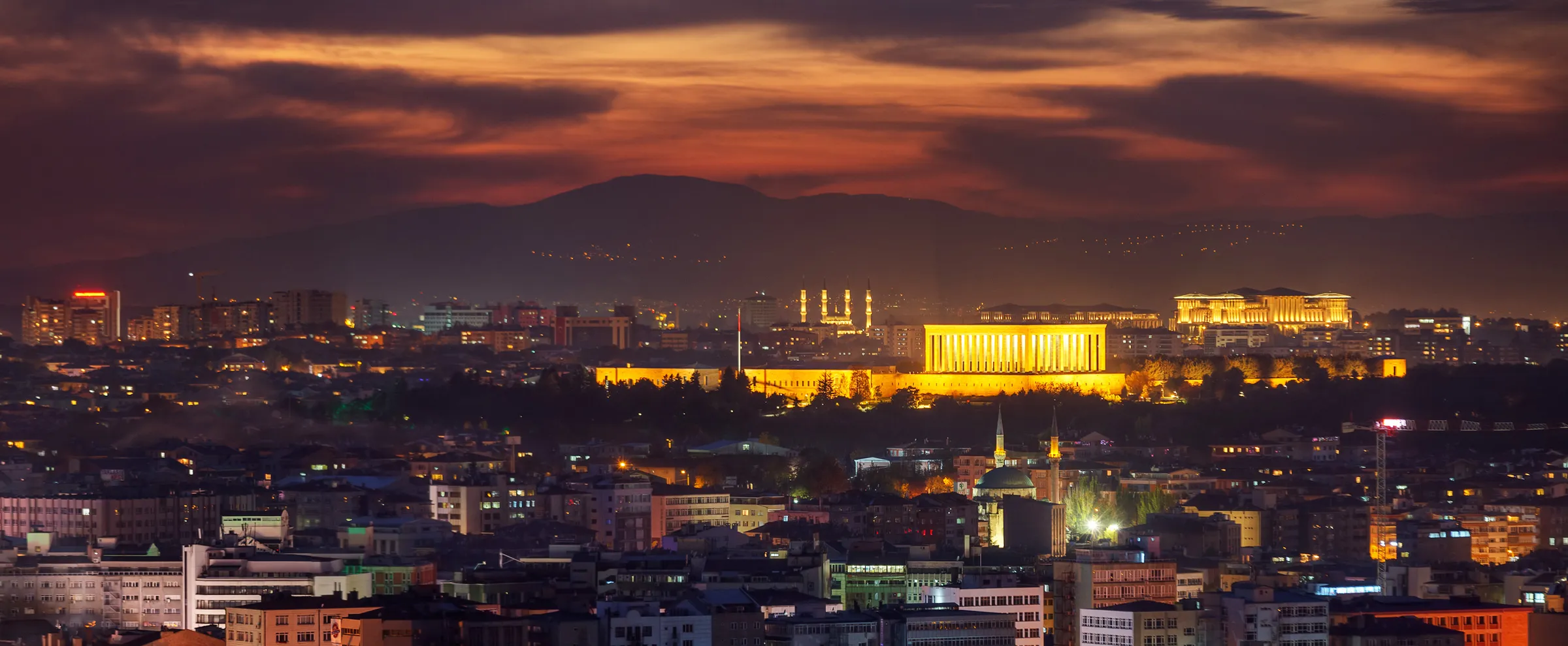 Ankara silüetinde gün batımı, arkada aydınlatılmış binalar ve dağlar.
