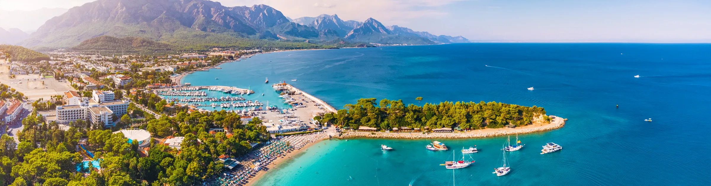 Antalya coastline with a marina, beach, and mountains, perfect for car rental road trips in Turkey.