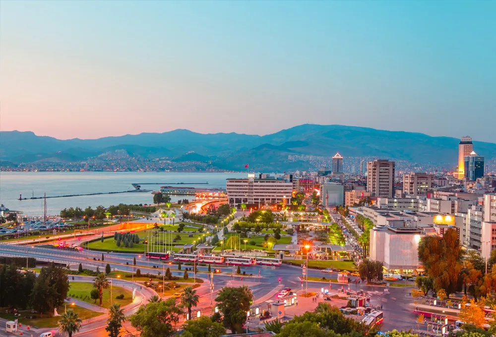 Vue sur la ville d'Izmir au coucher du soleil avec routes côtières, parfaite pour la location de voitures.
