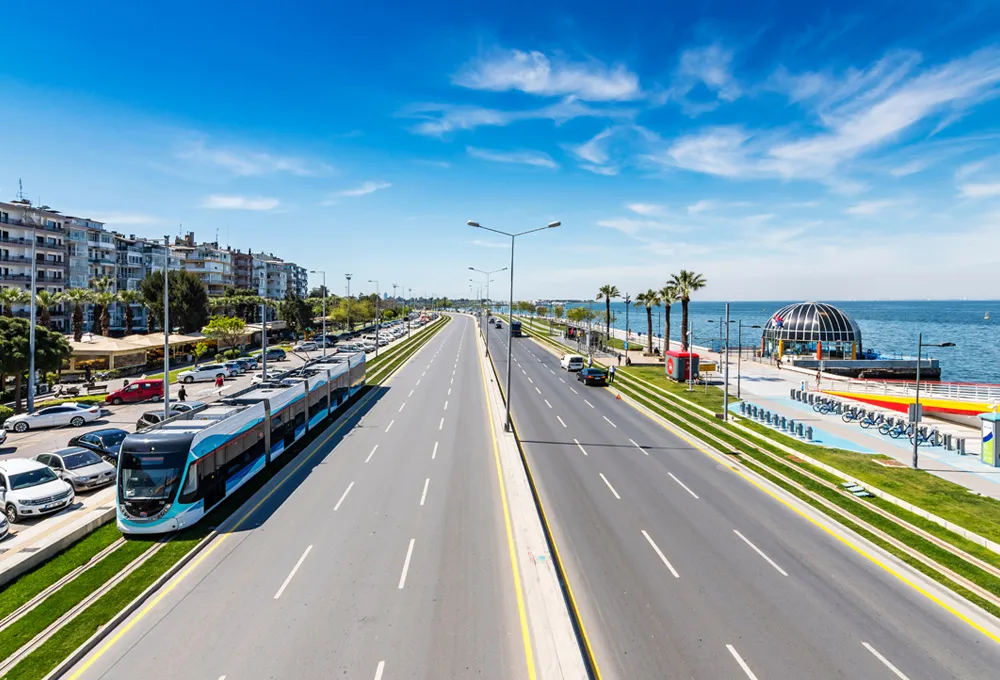 Route côtière avec voies de tram et bâtiments modernes le long du rivage sous un ciel bleu clair.