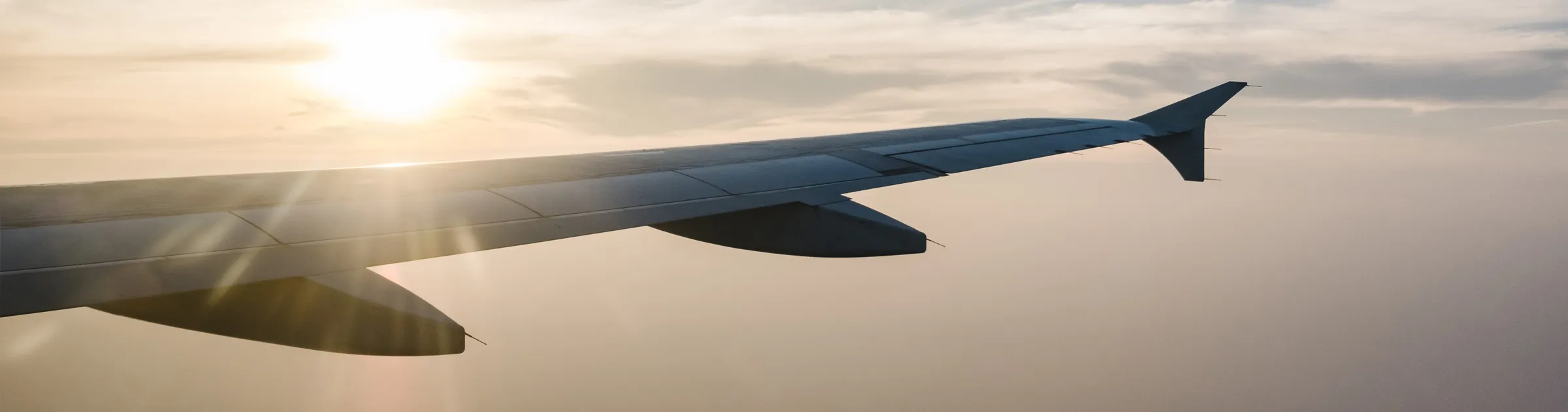 Ala di un aereo con il sole che brilla durante il volo sopra le nuvole al tramonto.