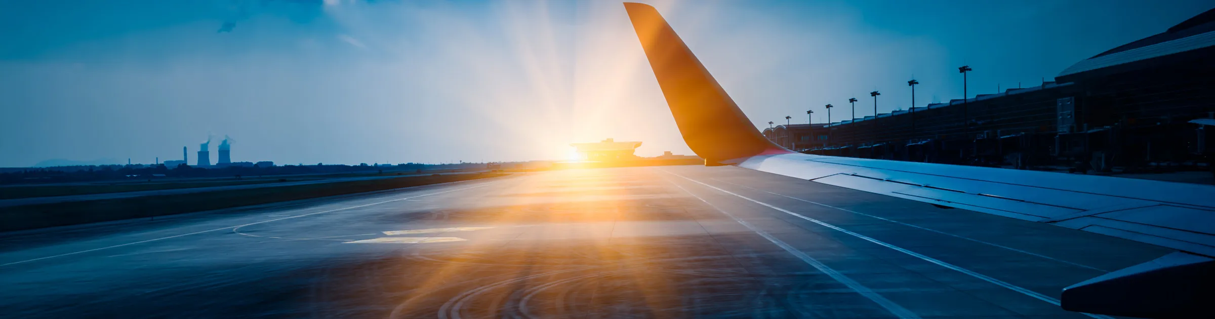 Airport runway at sunrise with an airplane wing and terminal building visible.