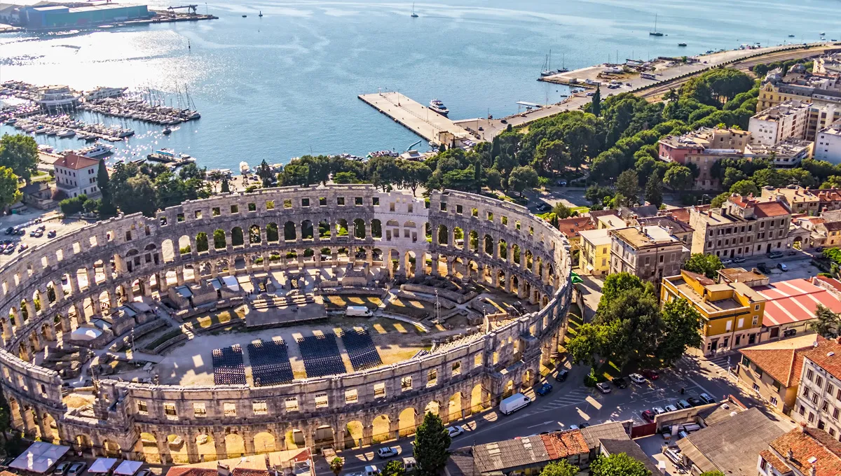 Pula Arena in Croatia near the waterfront and city buildings under clear sky.