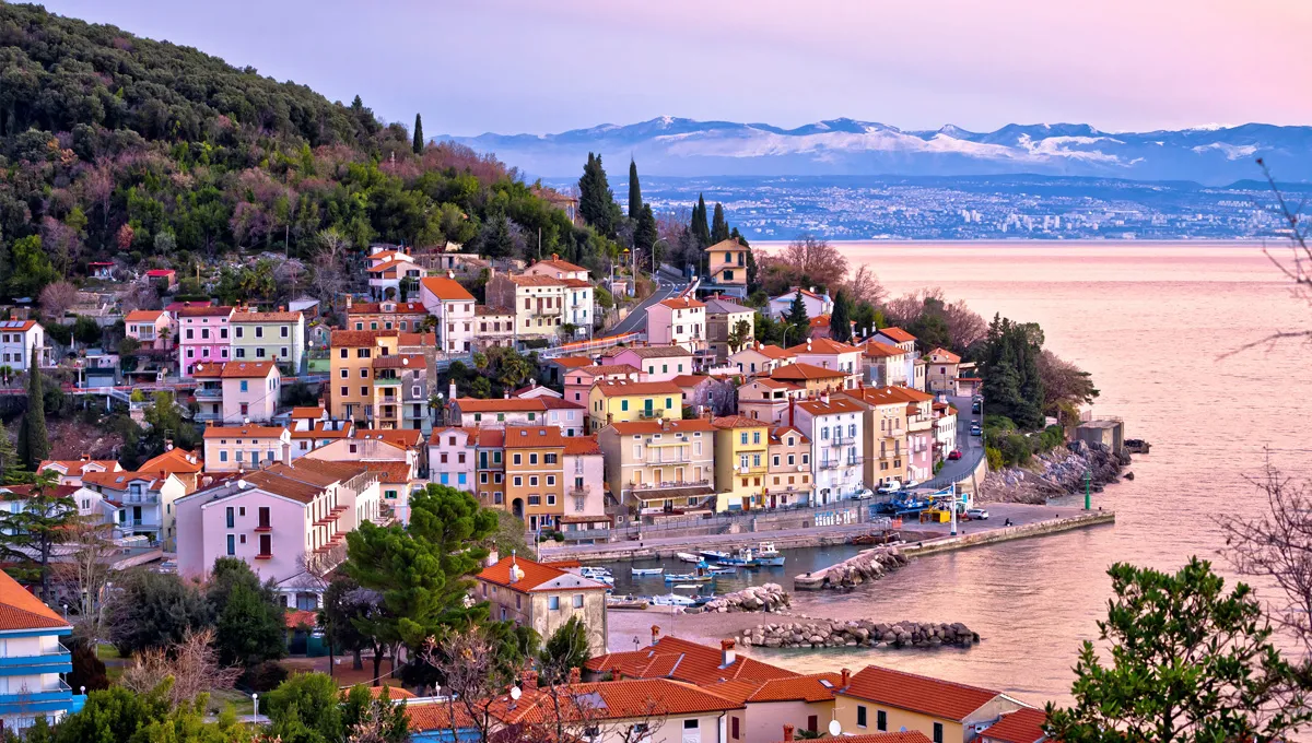 Coastal town with colorful houses by the sea and hills, ideal for car rental exploration.