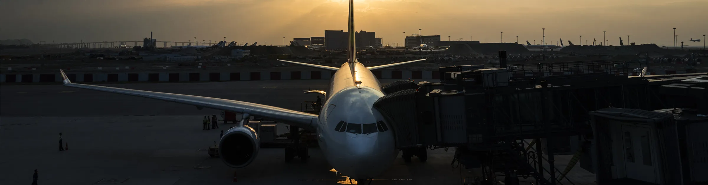 Vliegtuig geparkeerd bij luchthaven gate tijdens zonsondergang met andere vliegtuigen op de achtergrond.