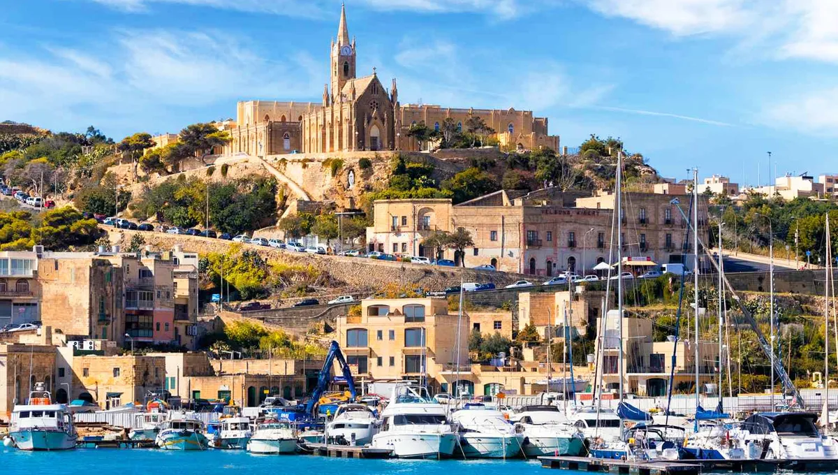 Senglea harbor in Malta with boats docked and the historic church atop the hill on a sunny day.
