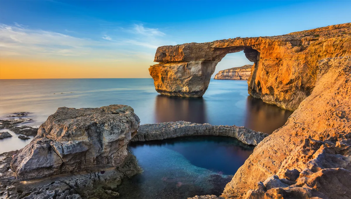 Azure Window limestone arch on Gozo, Malta, with calm sea and sunset sky visible.