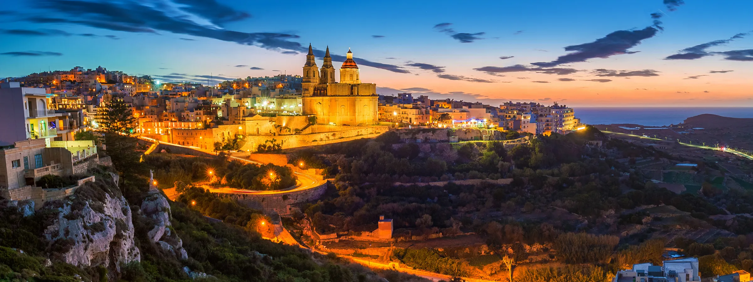 Mdina cityscape in Malta at sunset with historic buildings and winding illuminated roads.