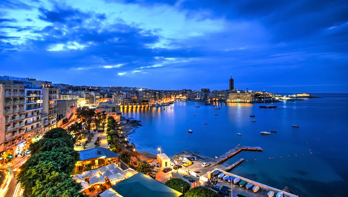 Malta waterfront cityscape at dusk with illuminated buildings and calm sea harbor view for car rental.