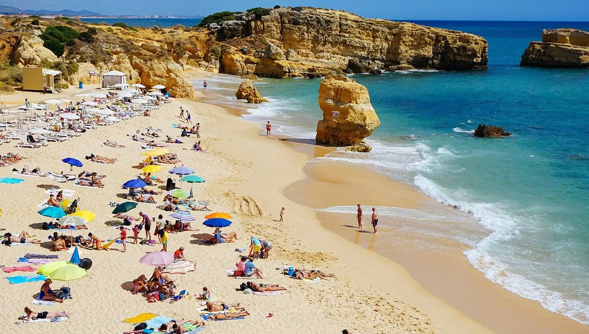 Algarve beach with sunbathers under umbrellas enjoying the sun by the sea.