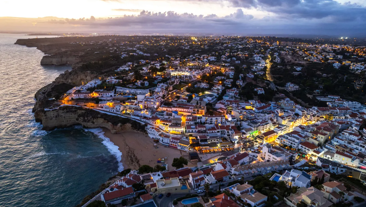 Carvoeiro town coastline in Portugal with illuminated buildings and beach at dusk, perfect for car rental trips.