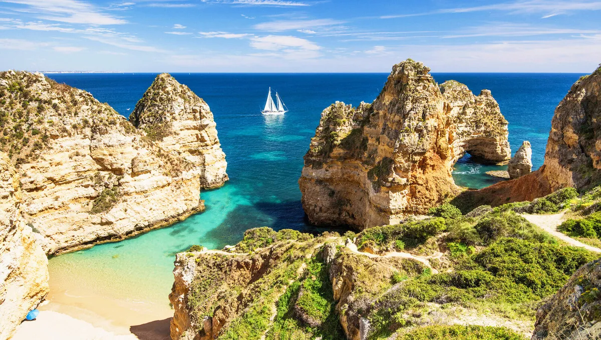Ponta da Piedade cliffs and beach with turquoise water and a white sailboat in Lagos, Algarve.