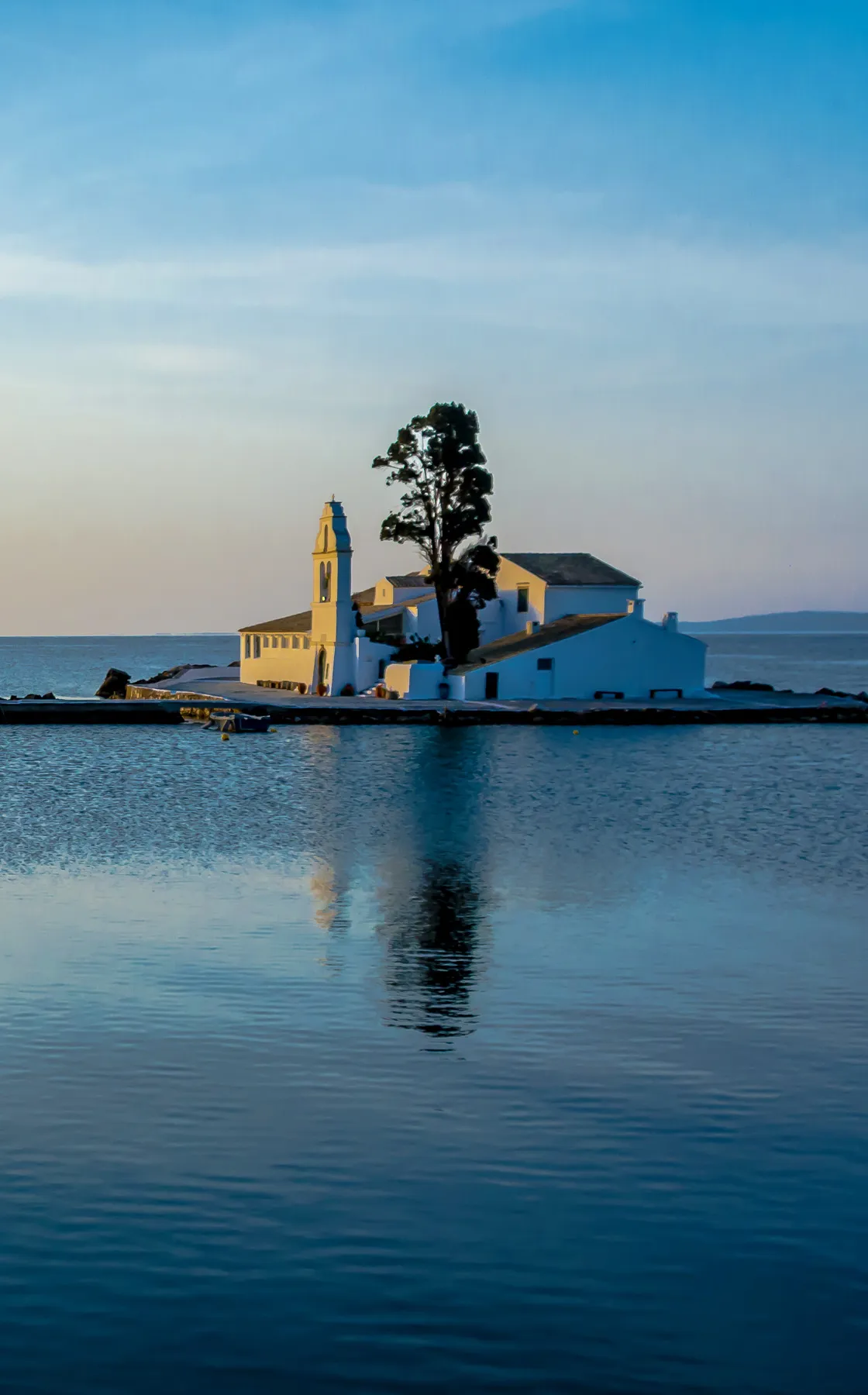 Small white coastal church with a bell tower on a peaceful island surrounded by calm blue sea.