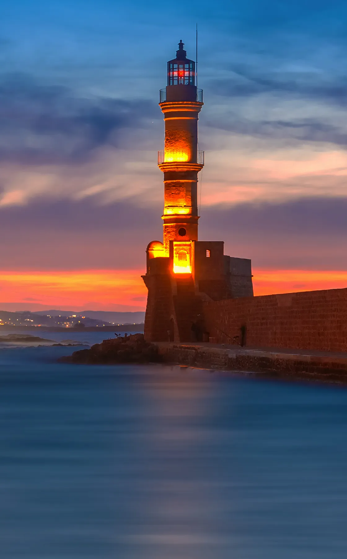 Chania lighthouse glowing warmly at sunset by the calm sea in Crete, Greece.