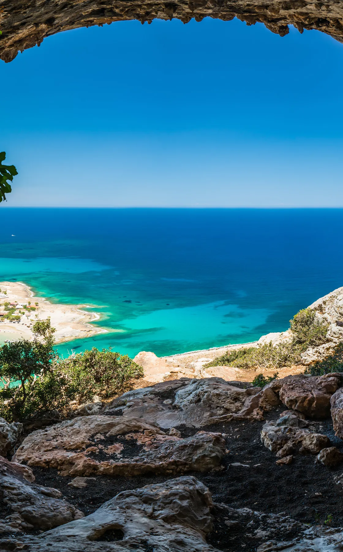 Sea view of a beach and clear blue water seen from a rocky cave opening at a coastal location.