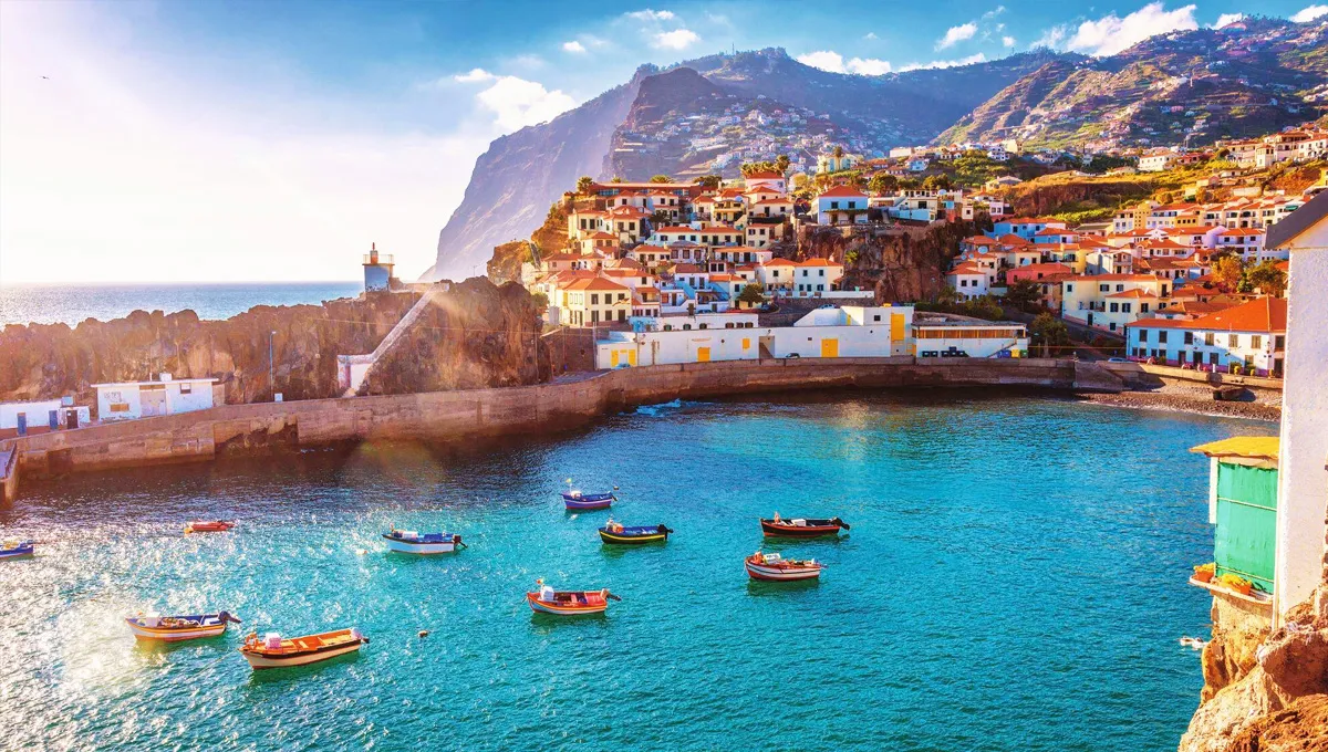 Costa da Madeira com casas coloridas em colinas e pequenos barcos numa baía solarenga.