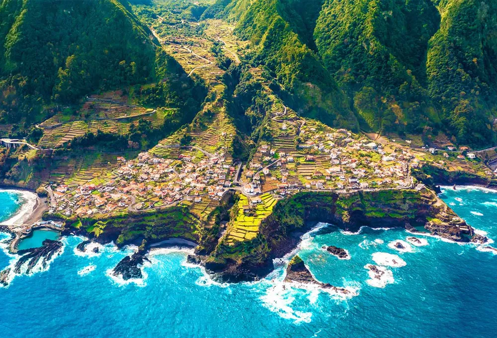 Costa da Madeira com montanhas verdes e vila costeira perto de água turquesa do oceano para viajar.