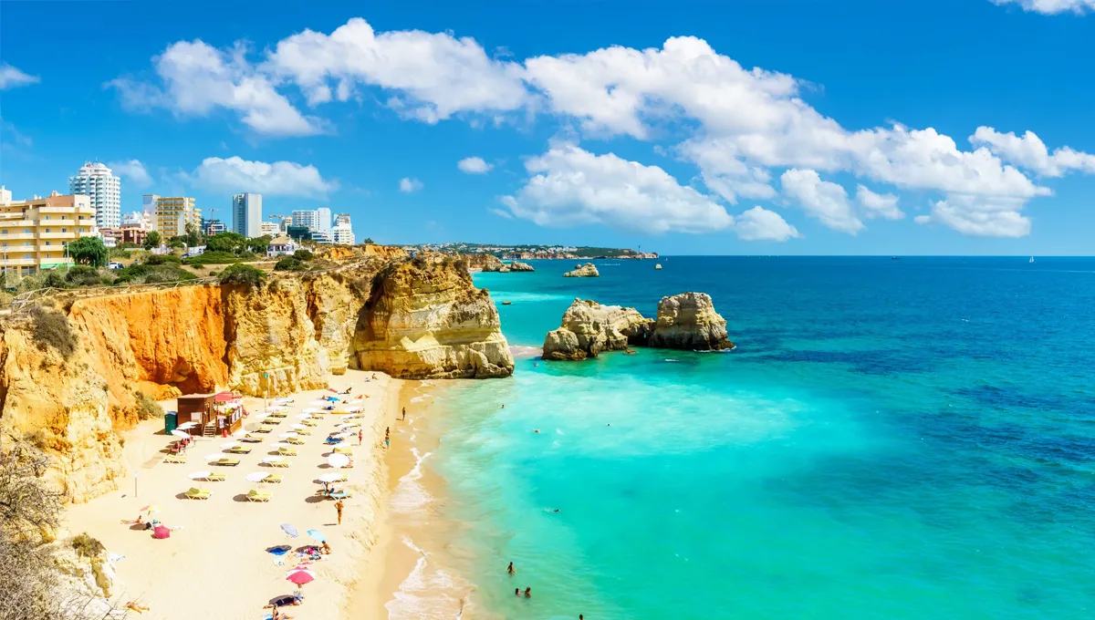 Lagos beach in Algarve with golden cliffs, turquoise sea, umbrellas, and sunbathers on a bright day.